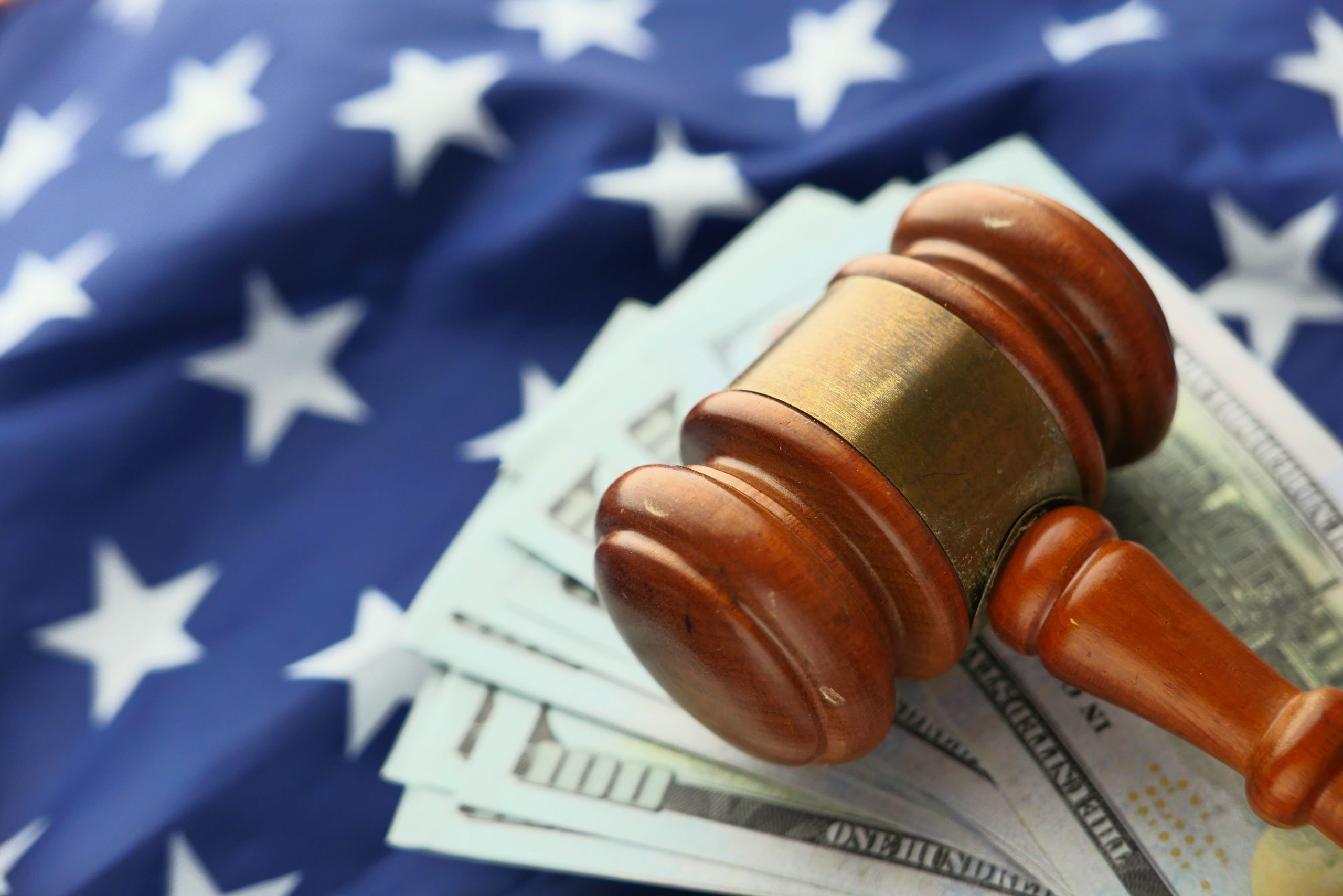 Close-up of a wooden gavel resting on US dollar bills against an American flag, symbolizing lawsuits and legal money battles
