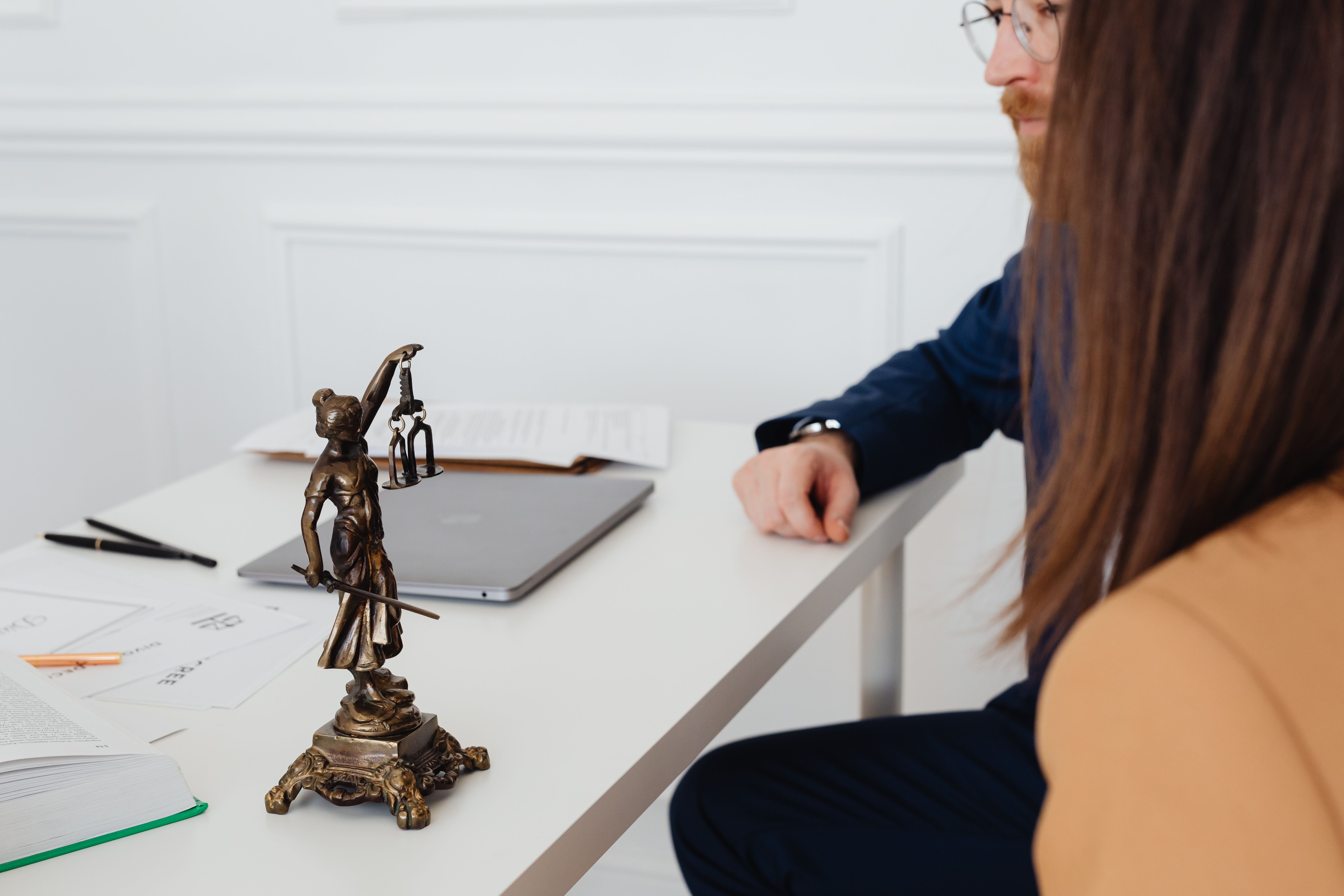 Lawyers discussing legal documents beside a Lady Justice statue in a professional office