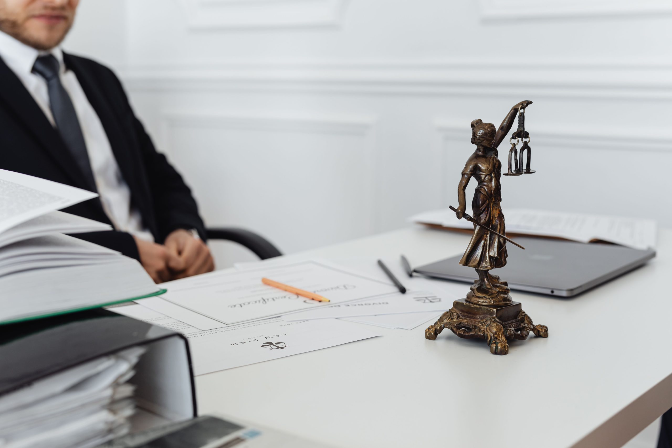 Lady Justice statue beside legal documents and a laptop on a lawyer's desk