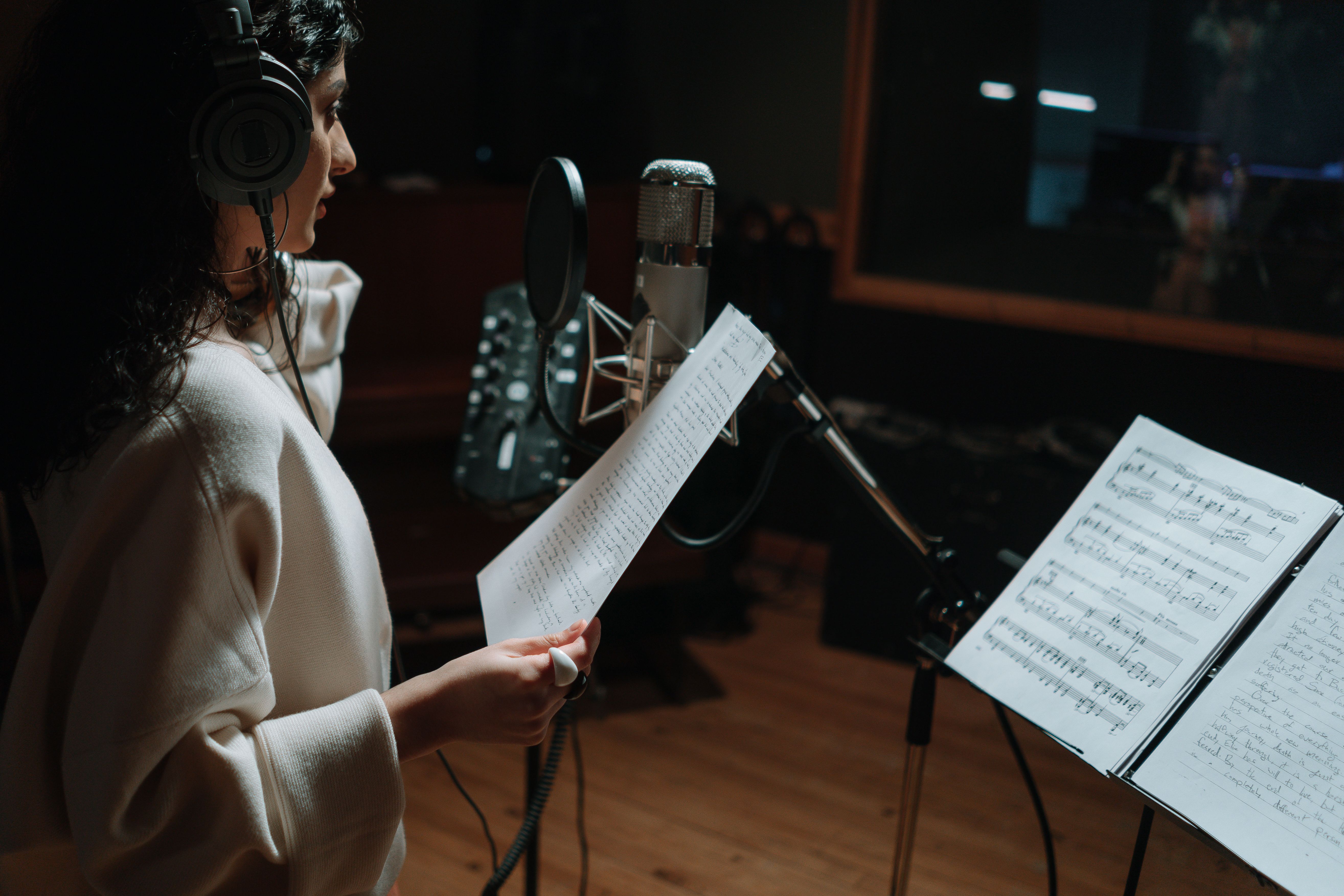 Singer recording vocals in a studio with a condenser microphone and headphones.
